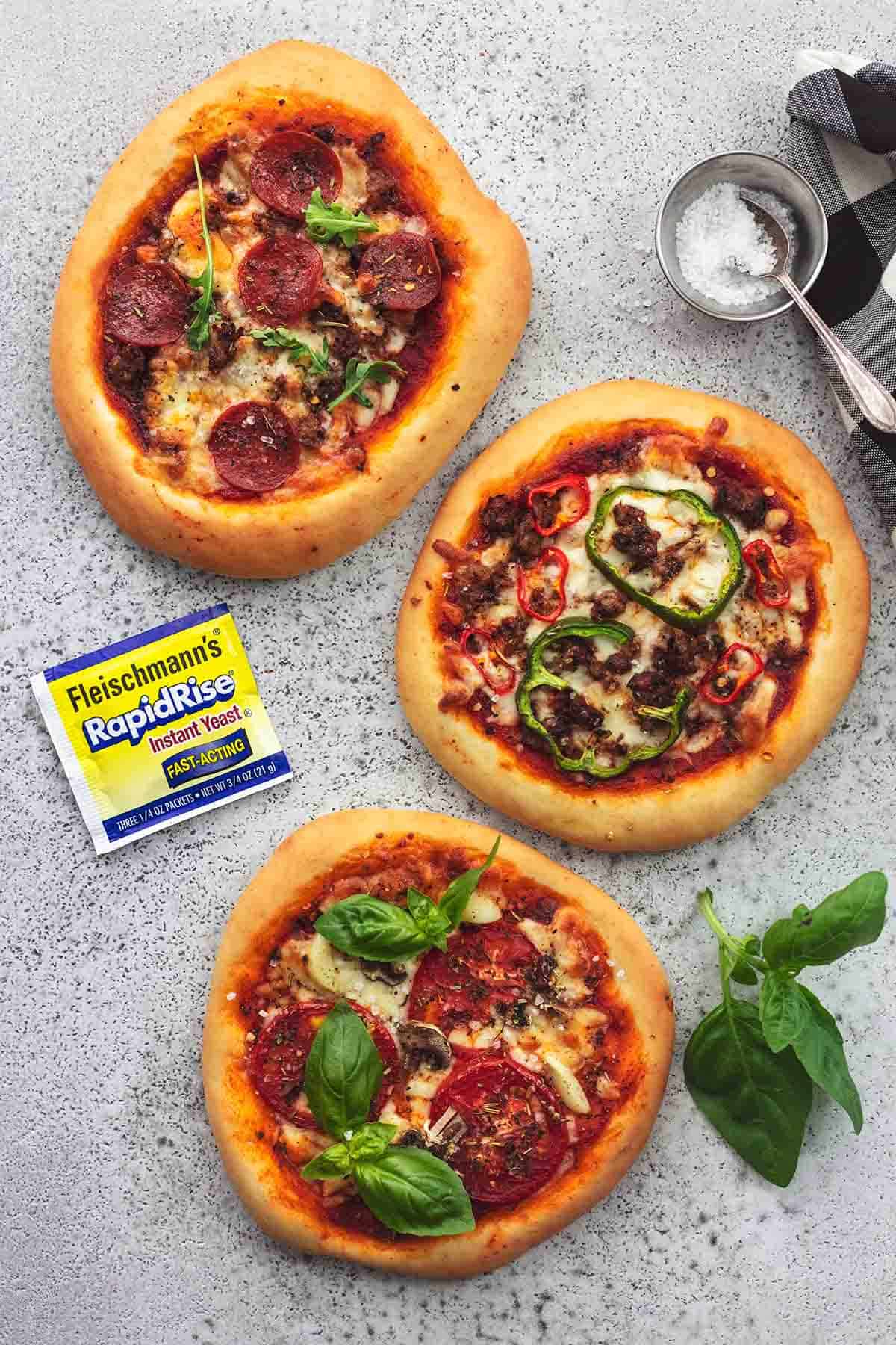 three small pizzas on gray surface with yeast packet on table 