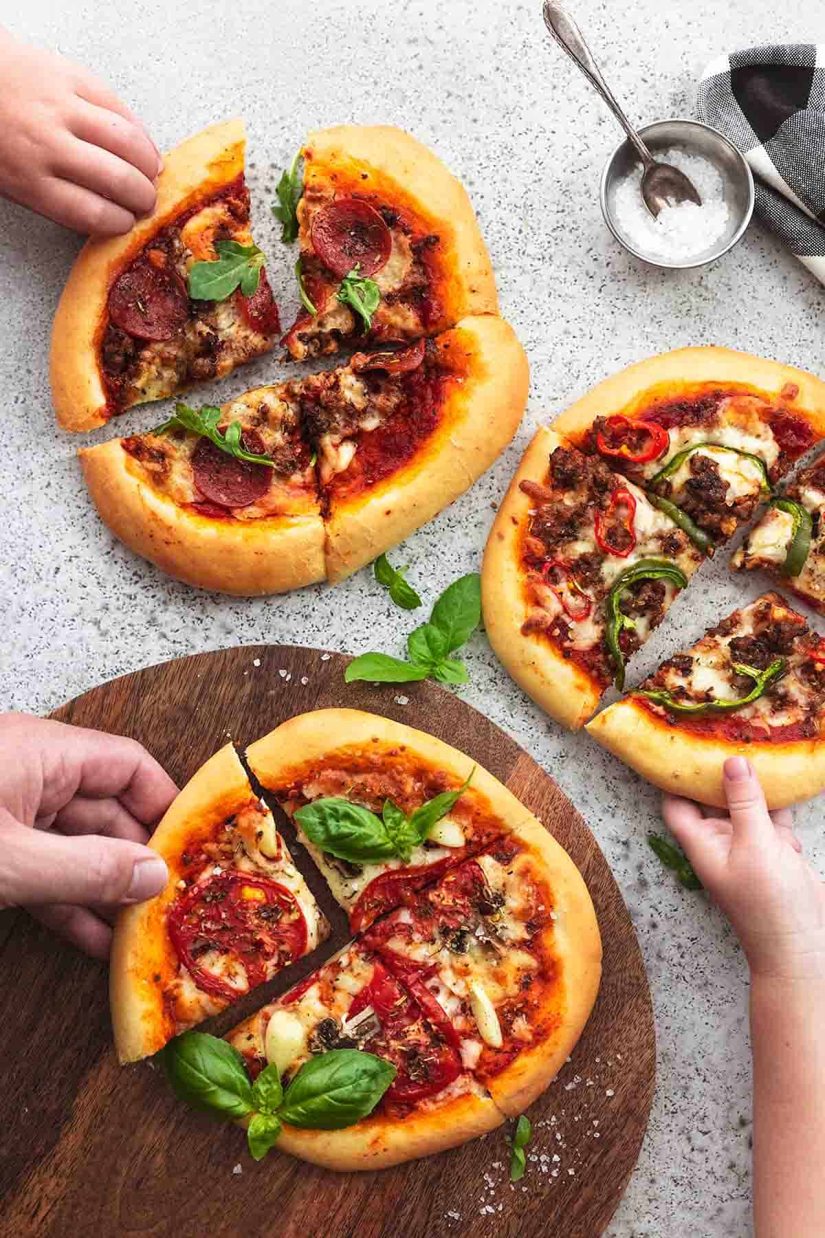 overhead view of one adult and two kid hands taking slices of pizza