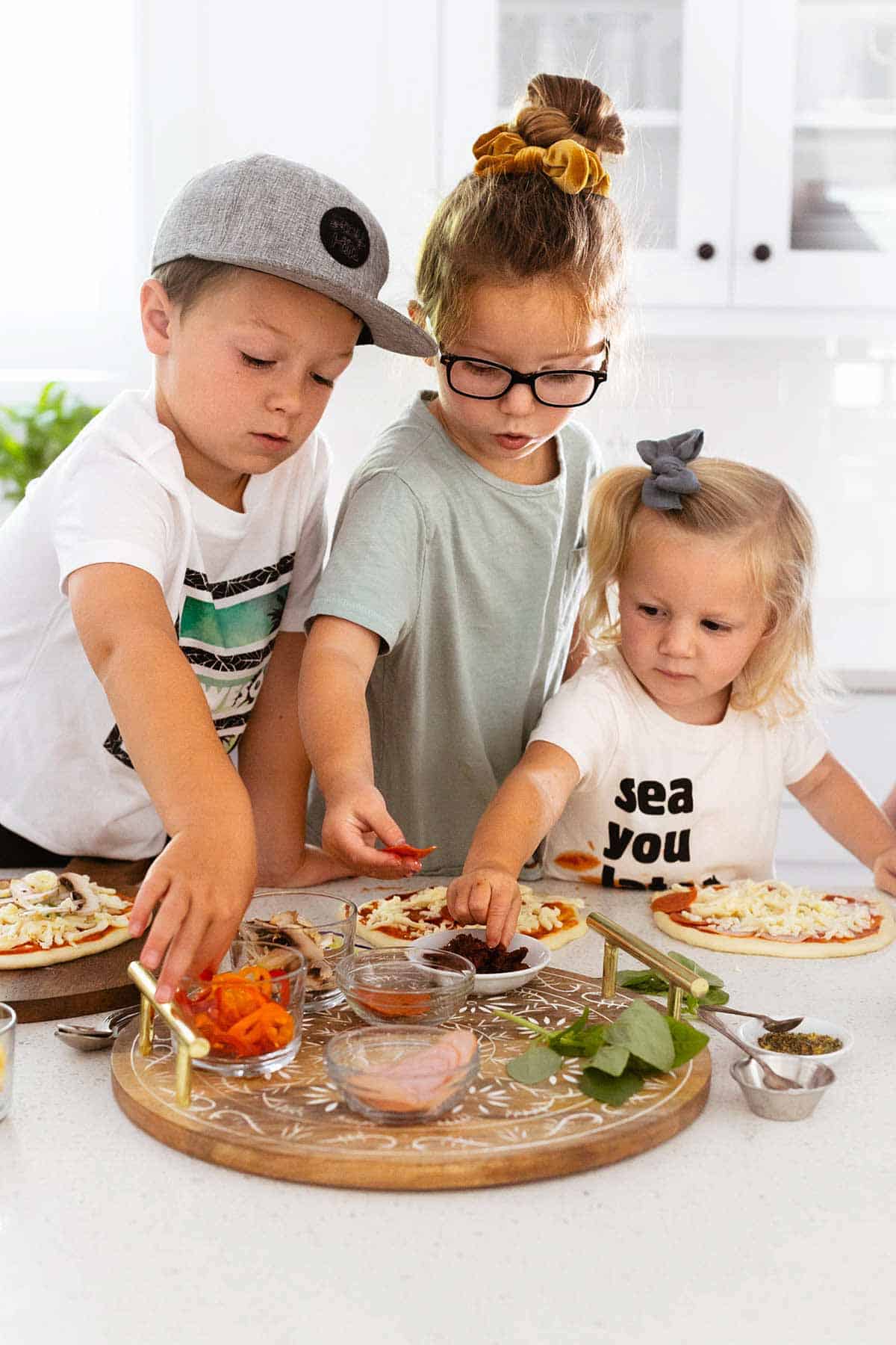 kids preparing personal pizzas in a kitchen. 