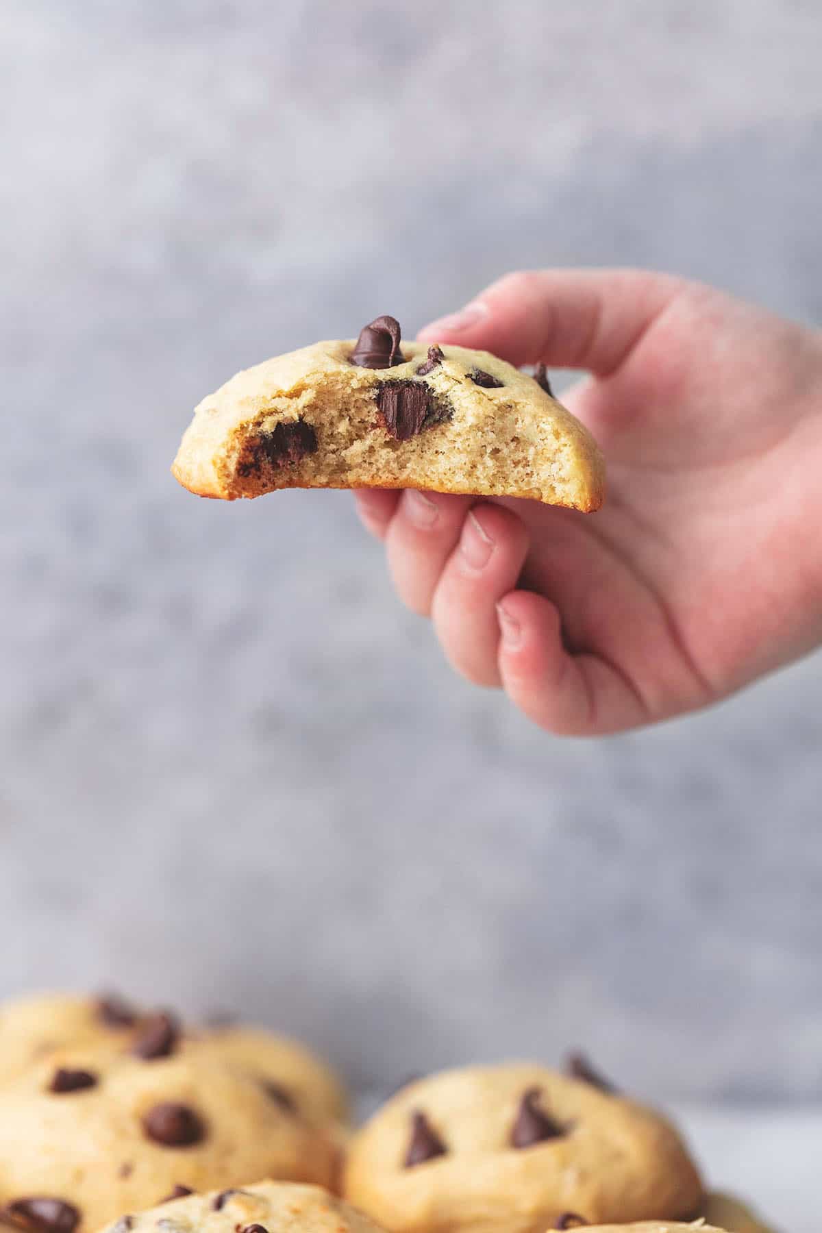 a child's hand holding half of a banana chocolate chip cookie above more cookie