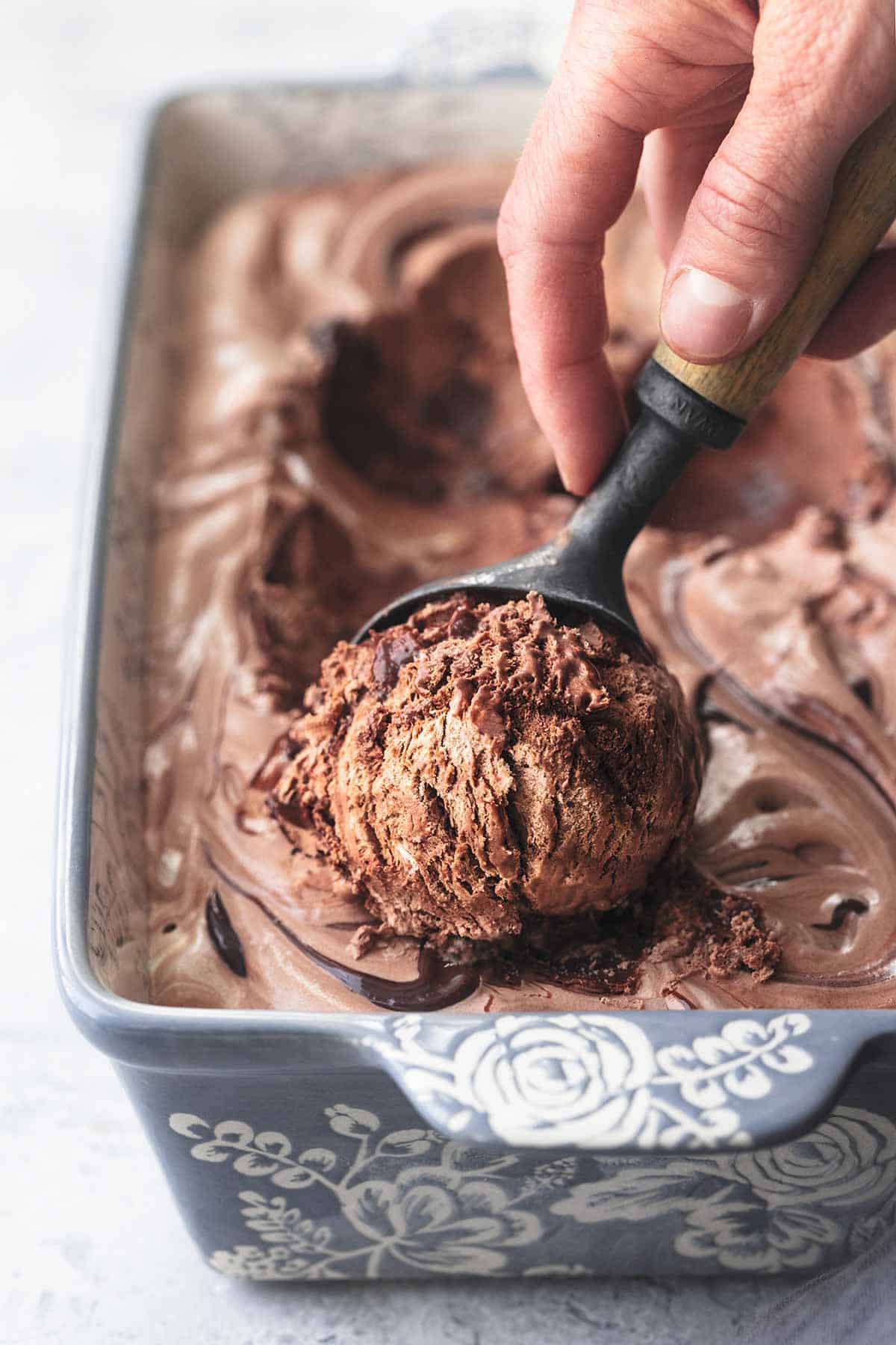 close up of a hand scooping fudge ripple chocolate ice cream with an ice cream scooper.
