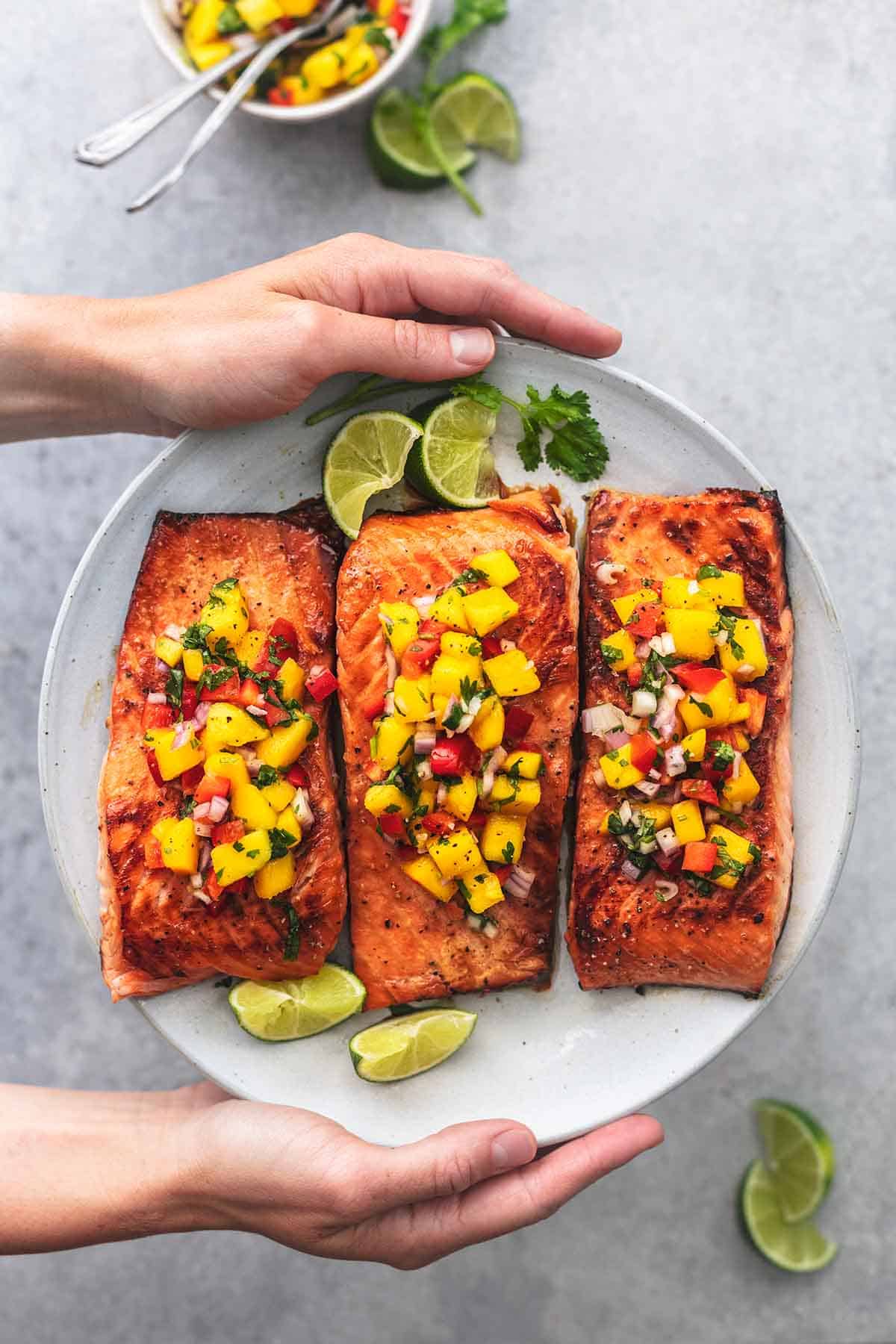 overhead hands holding plate of salmon topped with mango salsa