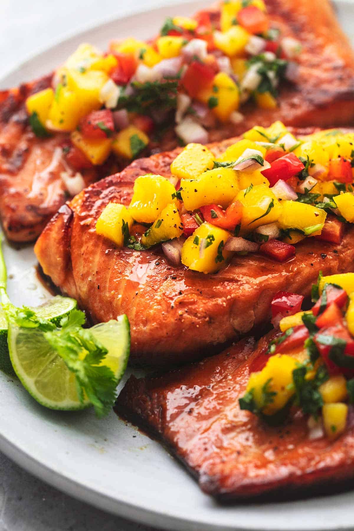 close up of honey lime salmon with mango salsa with lime slices on a plate.
