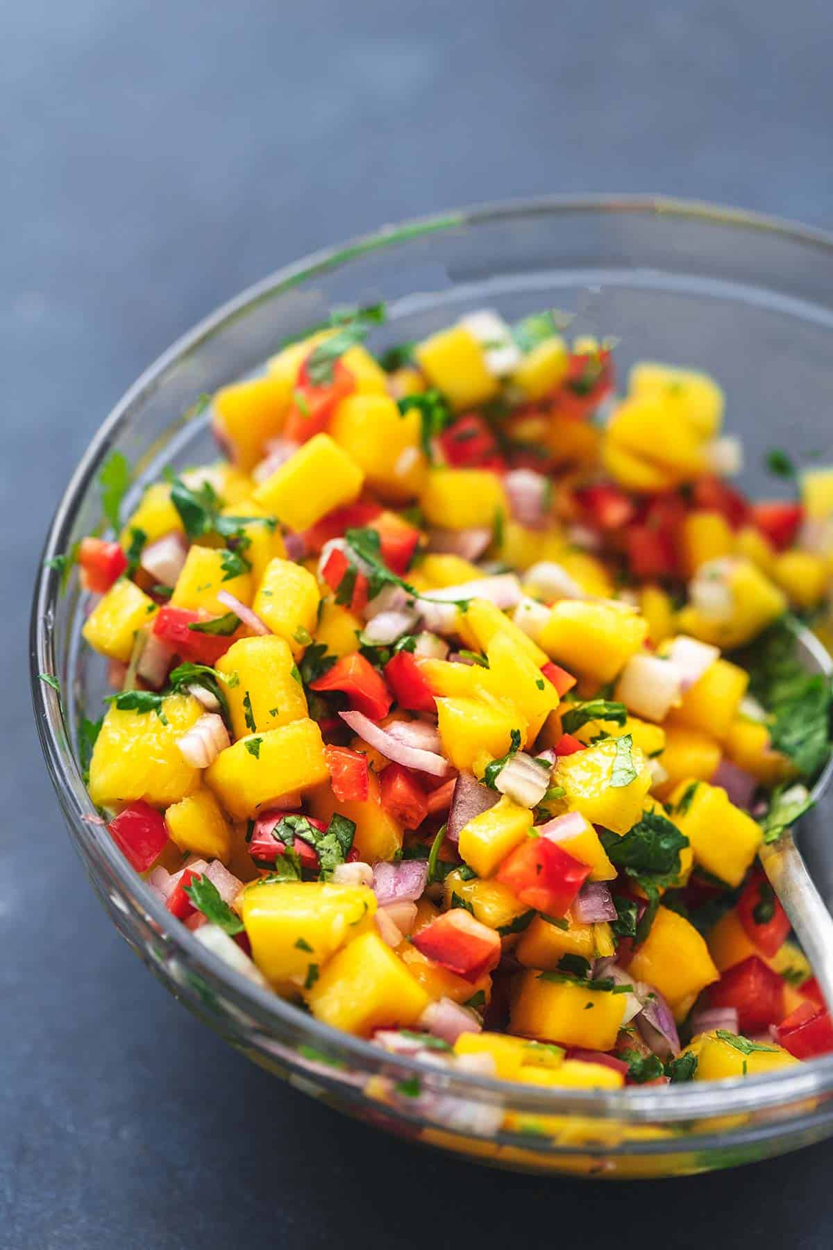 close up of mango salsa in a clear bowl with a spoon.