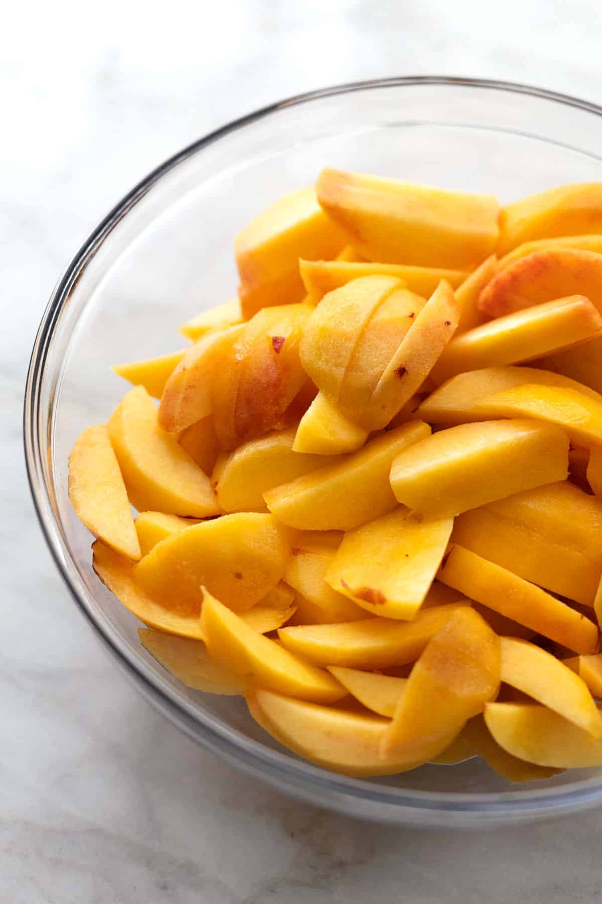 close up of peeled peach slices in glass bowl