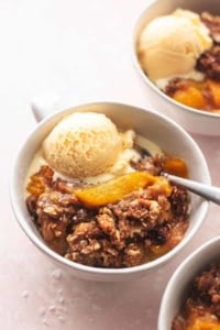 three bowls of peach crisp with spoons and vanilla ice cream