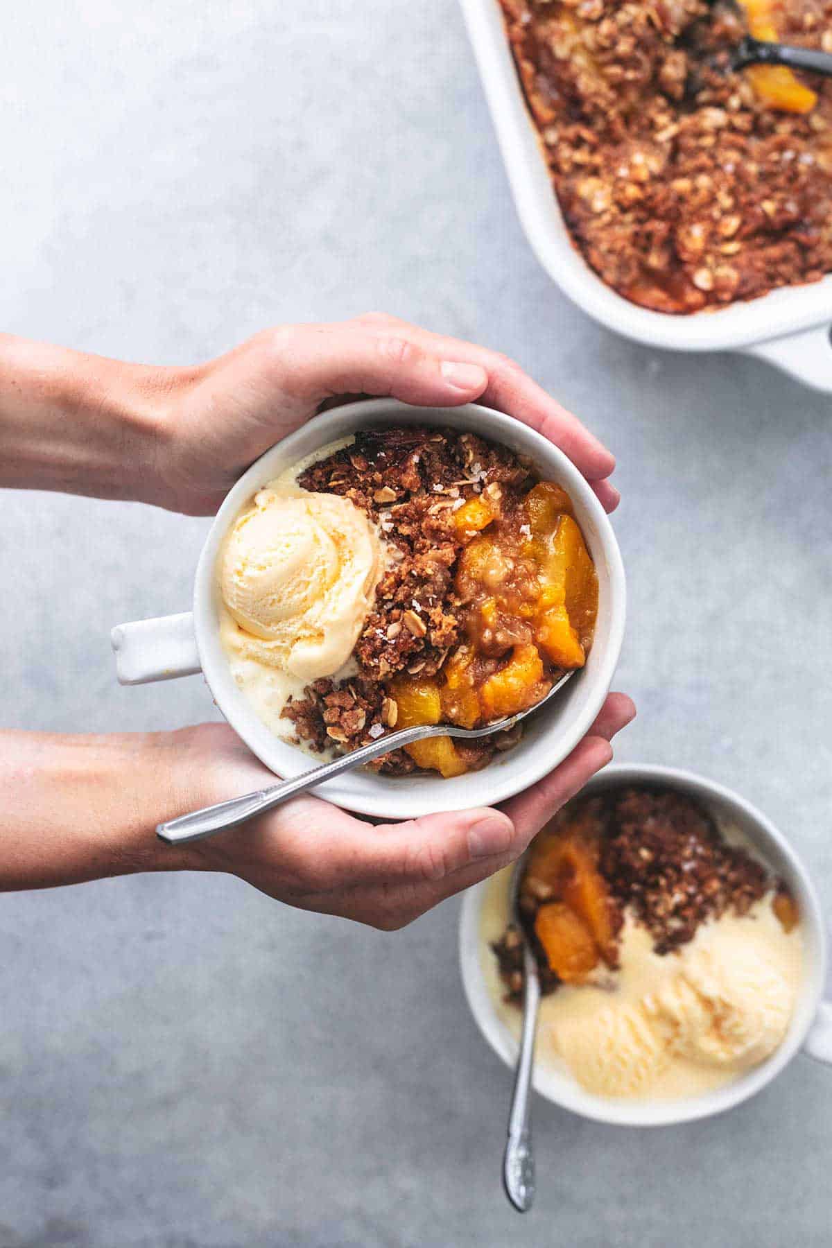 overhead view of hands holding bowl of peach crisp over two more bowls