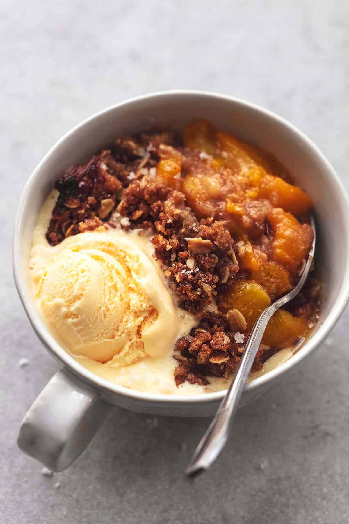 peach crisp with scoop of ice cream and a spoon in a bowl.