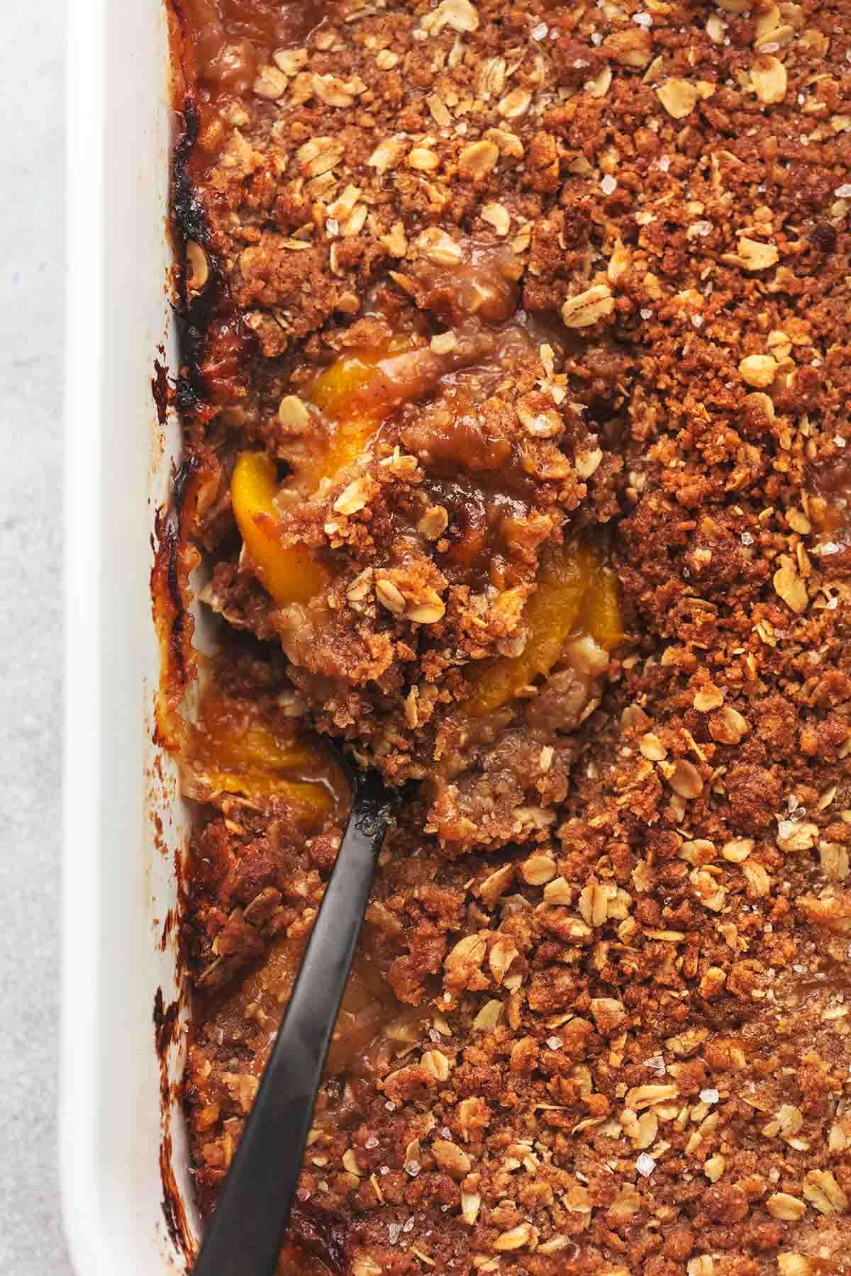 close up top view of a serving spoon in a pan of peach crisp.