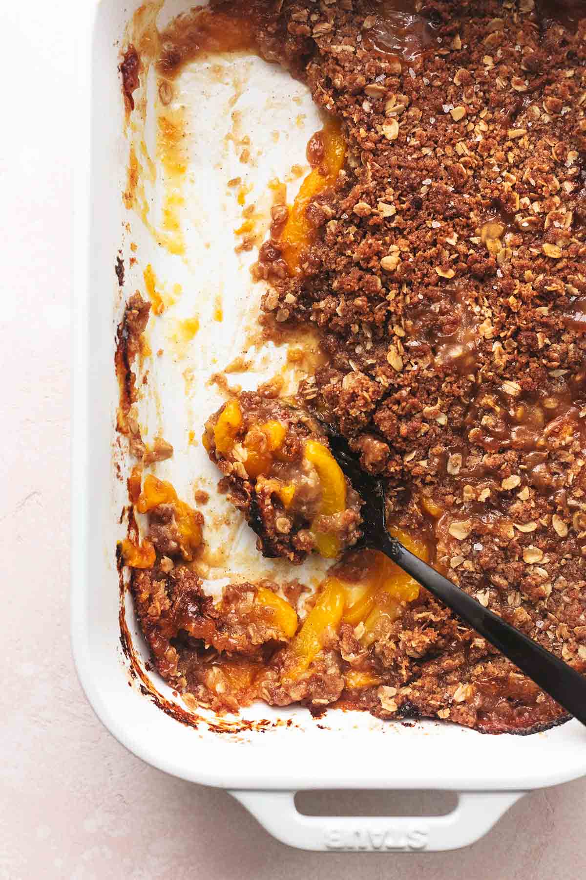 a serving spoon in a pan of peach crisp with some gone.