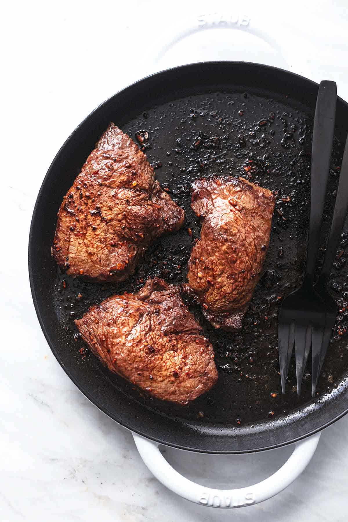 overhead view of three cooked steak in a white skillet