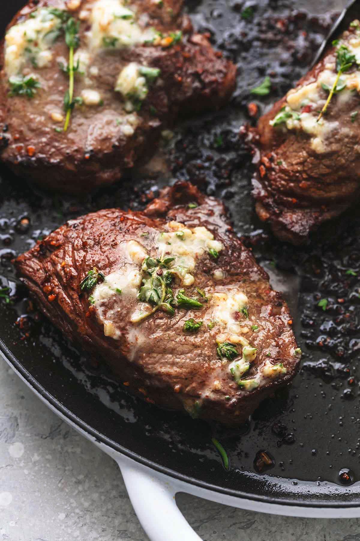 up close grilled steak on pan topped with butter and herbs