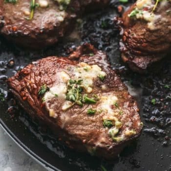 up close grilled steak on pan topped with butter and herbs