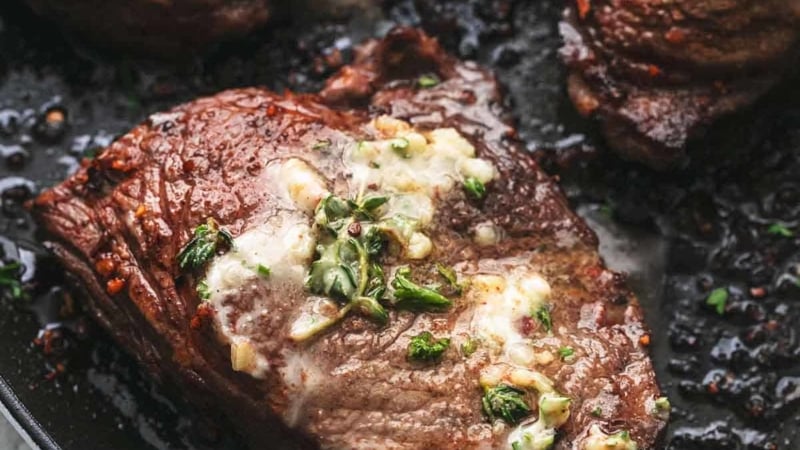 up close grilled steak on pan topped with butter and herbs