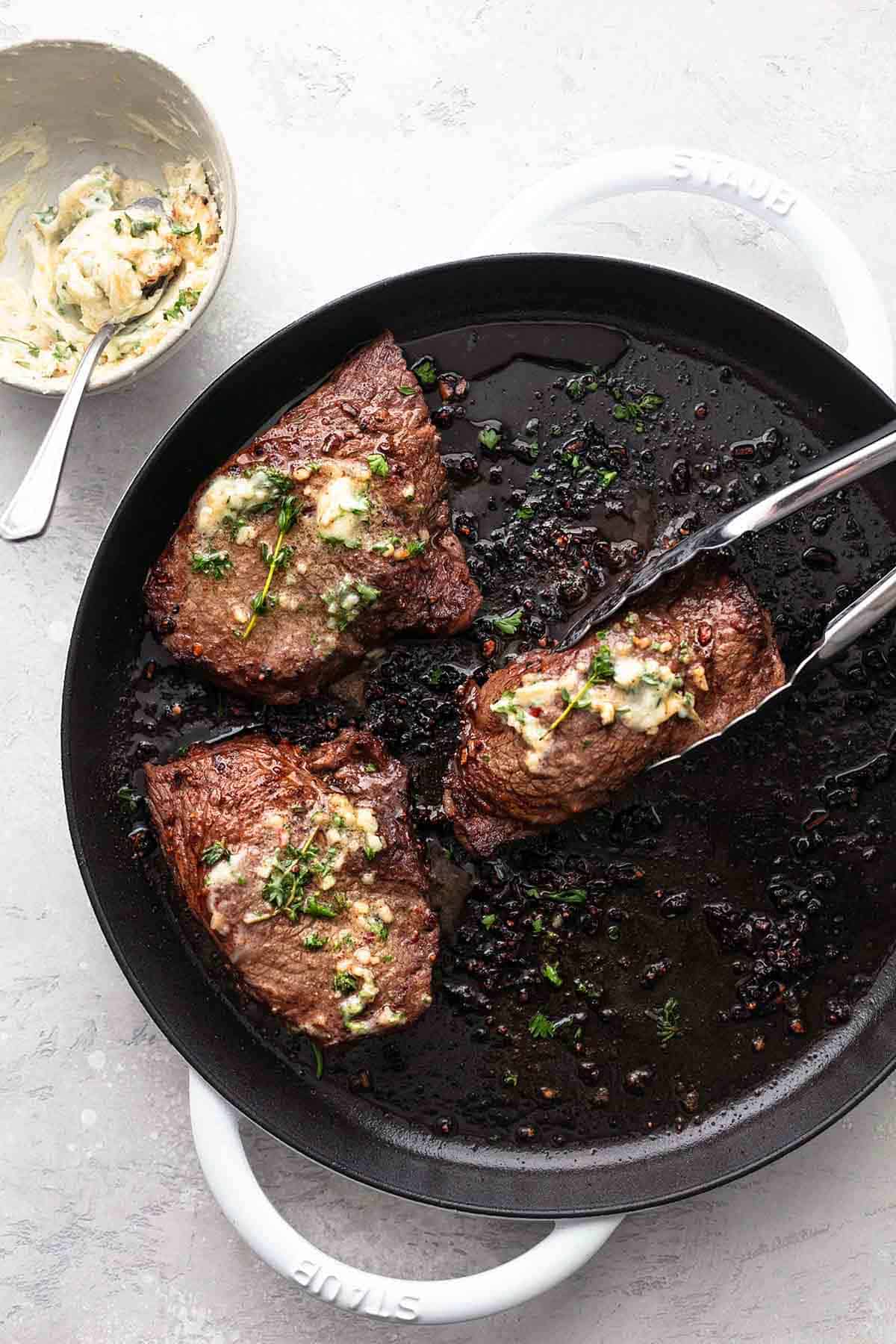 overhead three steaks on grill pan topped with butter