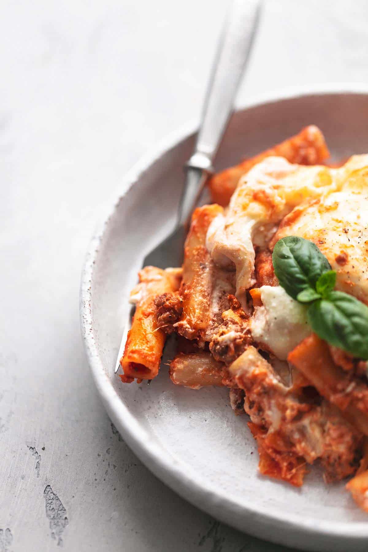close up of four cheese baked ziti on a fork with some more pasta on the side on a plate.