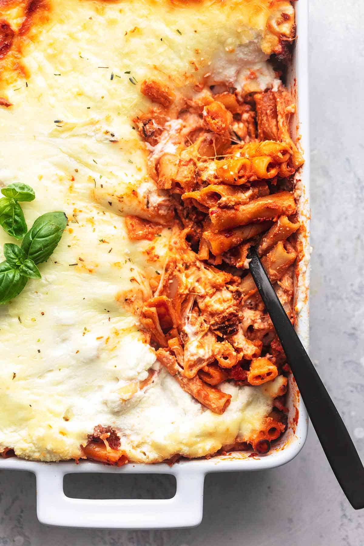 top view of four cheese baked ziti in a pan with a serving spoon dipping into the corner of the pan.