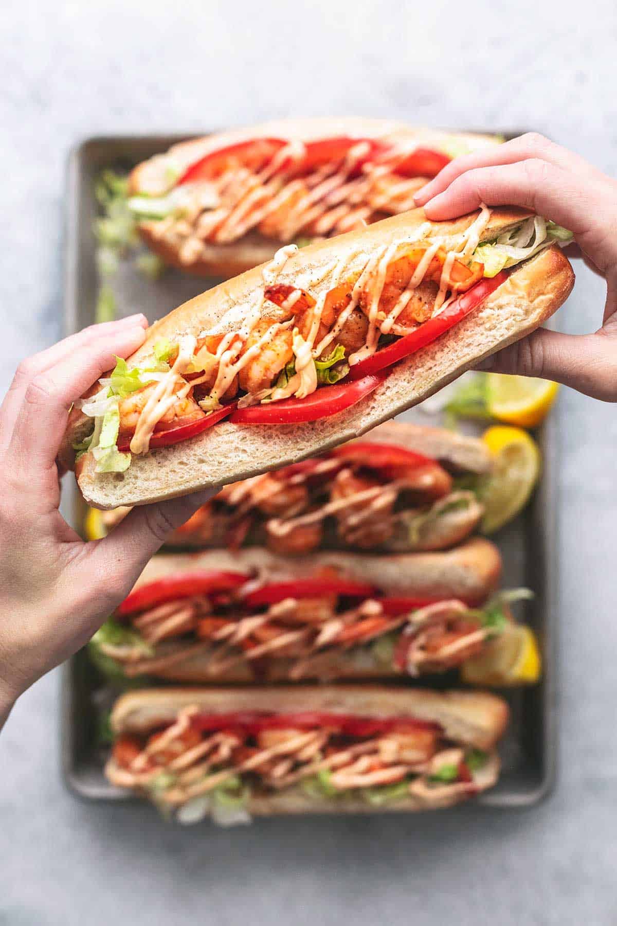 top view of hands holding a blackened shrimp po boy over a baking sheet of more.