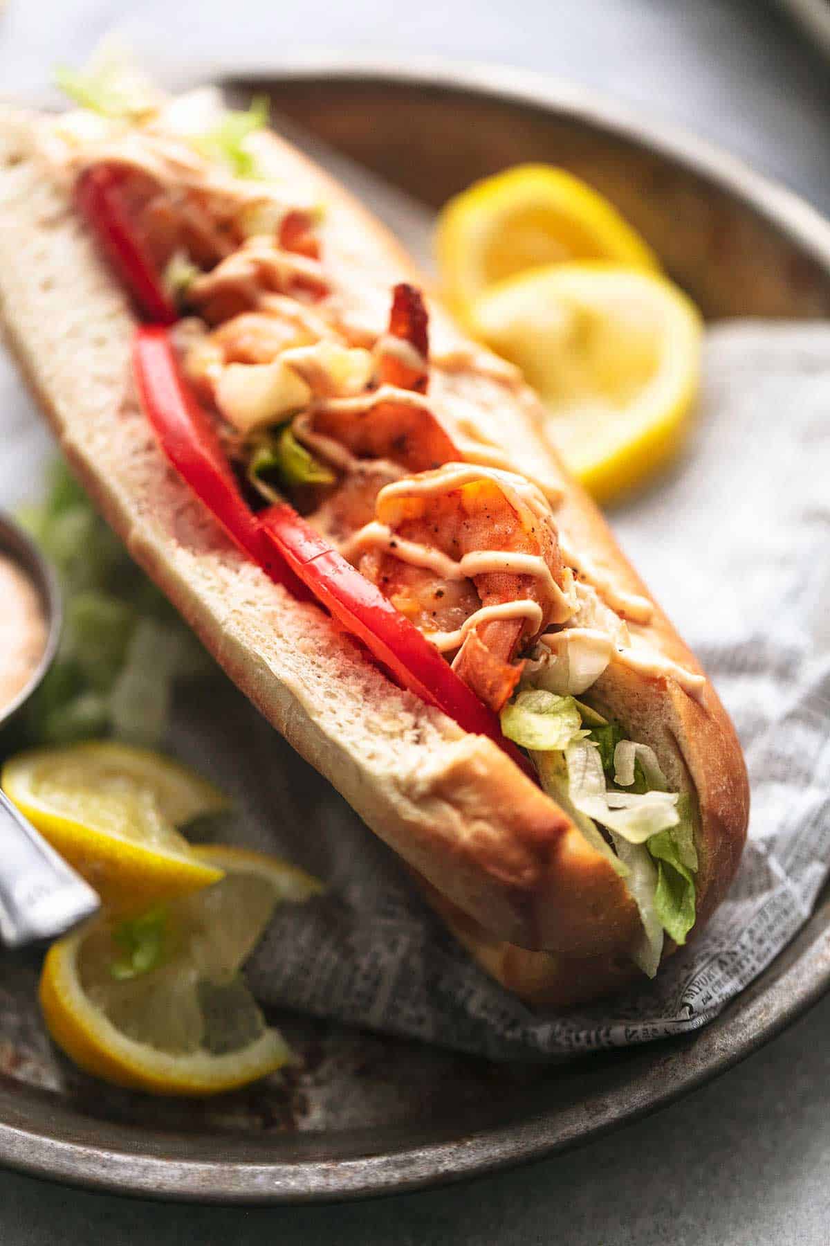 close up of a blackened shrimp po boy with lemon wedges on the side.