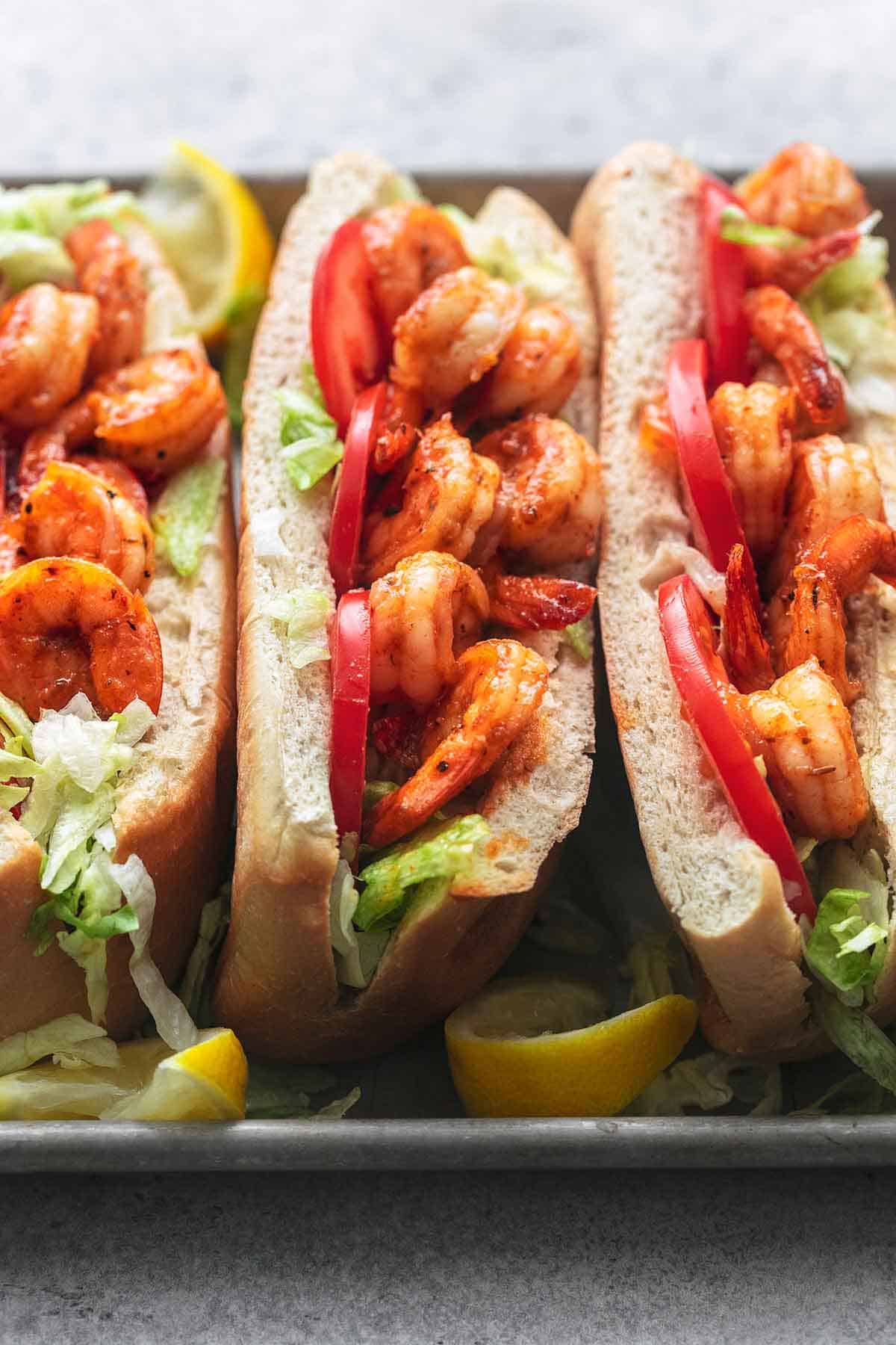 three split buns filled with cooked shrimp on a metal pan with lemons