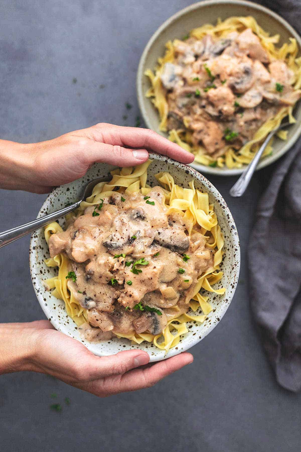 top view of hands holding a bowl of chicken stroganoff with a mother bowl on the side.