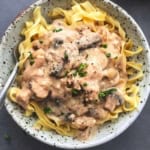 overhead view of saucy brown chicken and mushrooms over noodles in bowl with fork