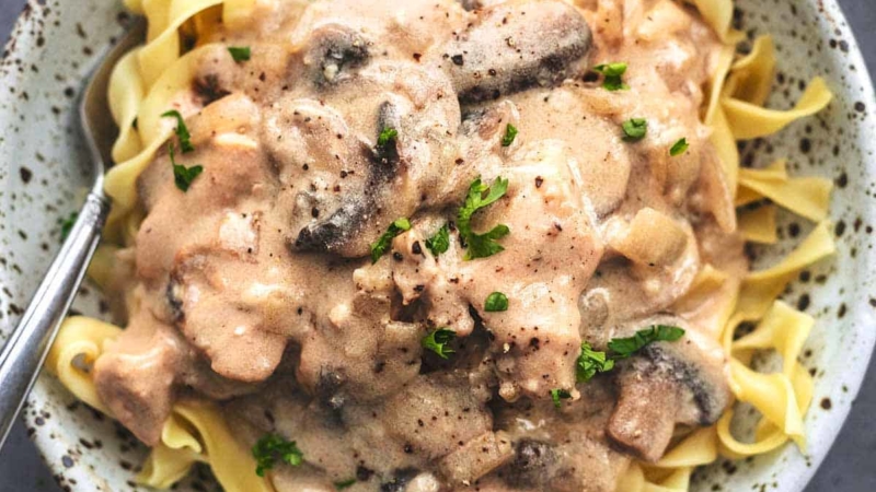 overhead view of saucy brown chicken and mushrooms over noodles in bowl with fork