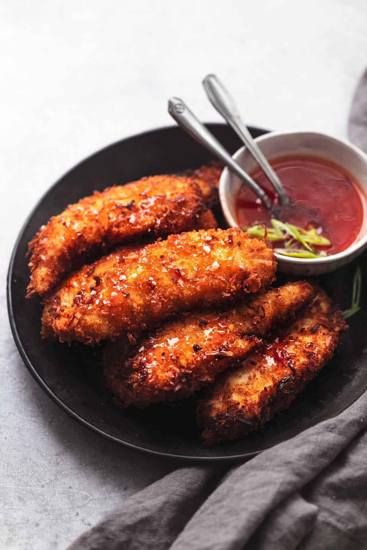 coconut chicken tenders on a black plate with red sauce in a bowl on the side.