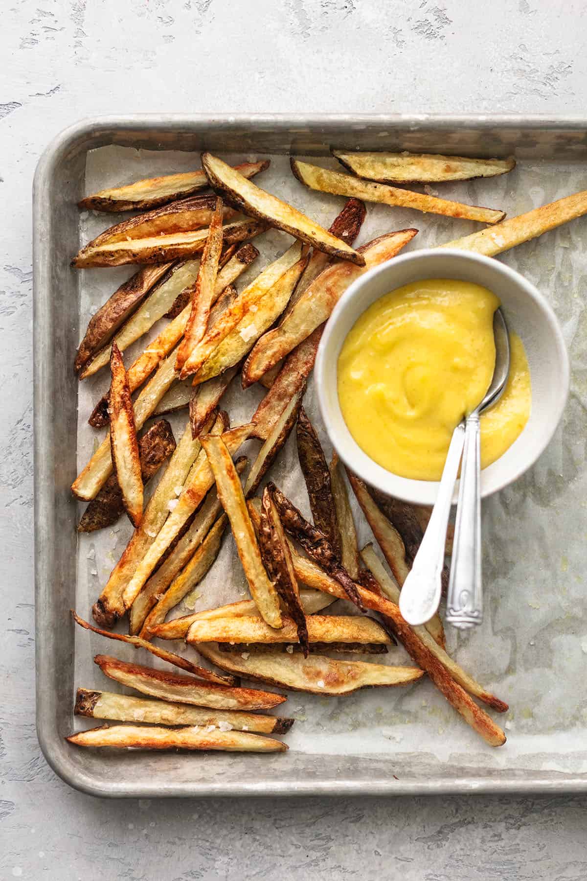 overhead view of sheet pan with crispy french fries and small bowl of garlic aioli
