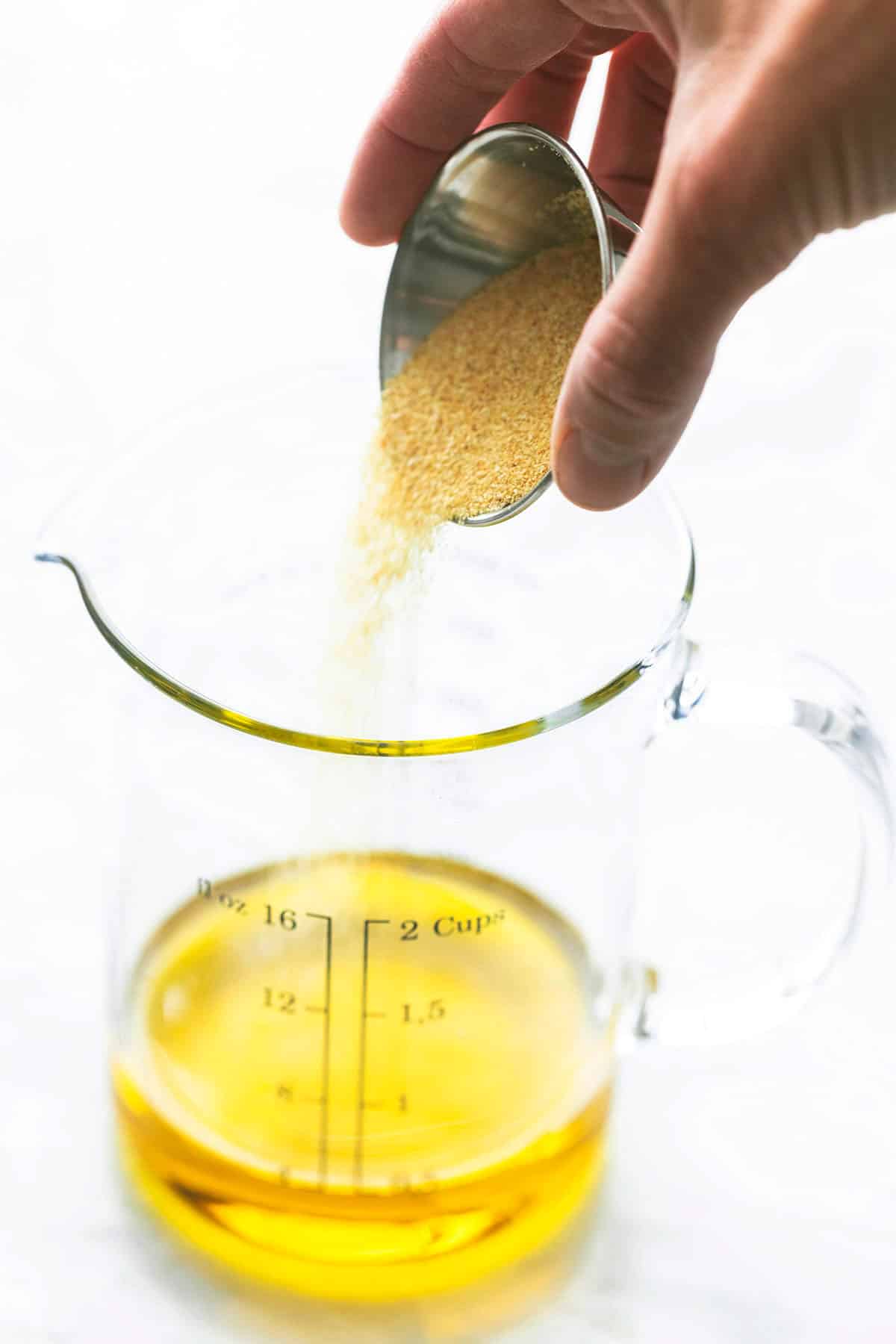 a hand pouring garlic powder into olive oil in a liquid measuring cup.