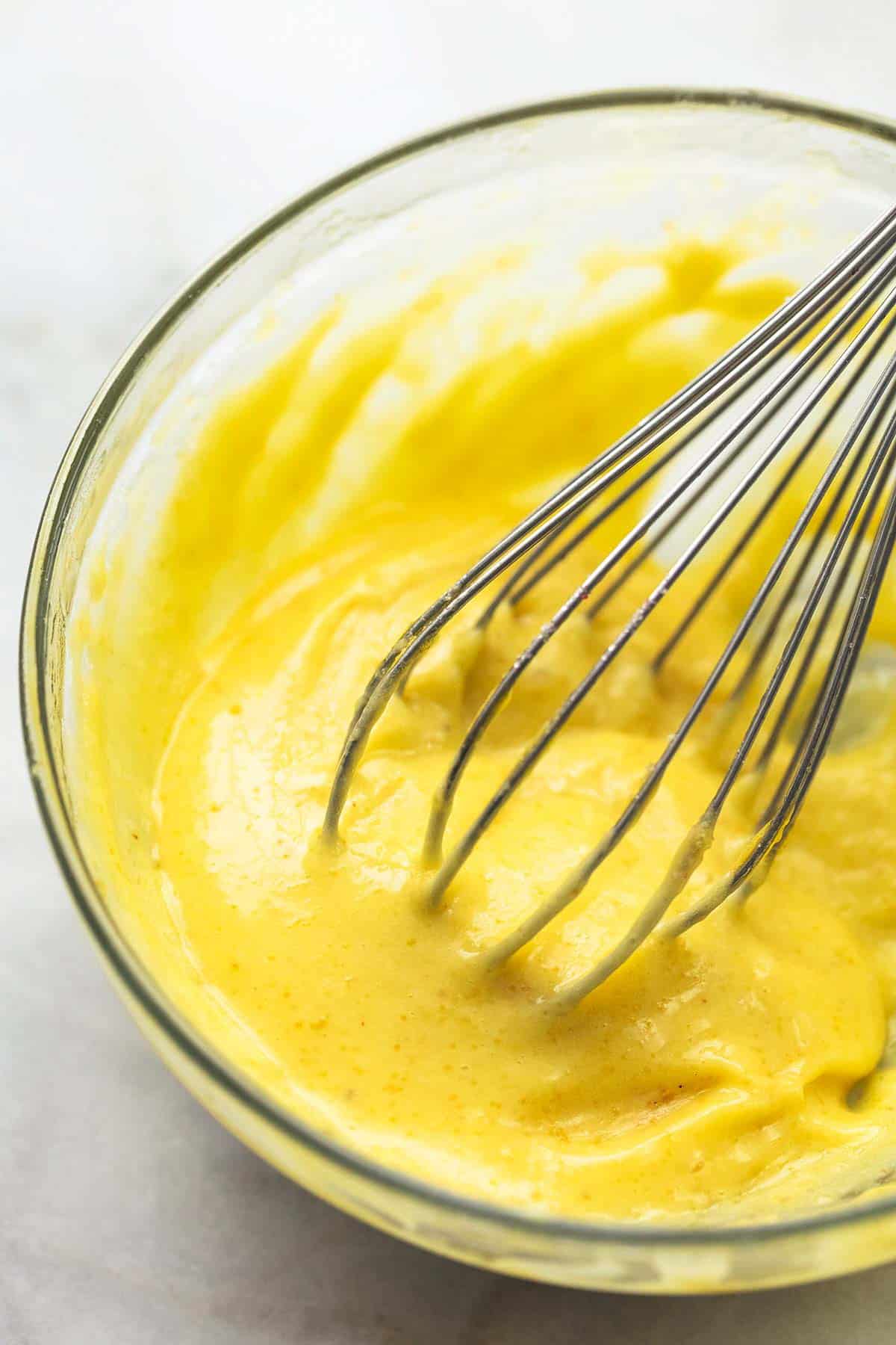 close up of garlic aioli with a whisk in a glass bowl.
