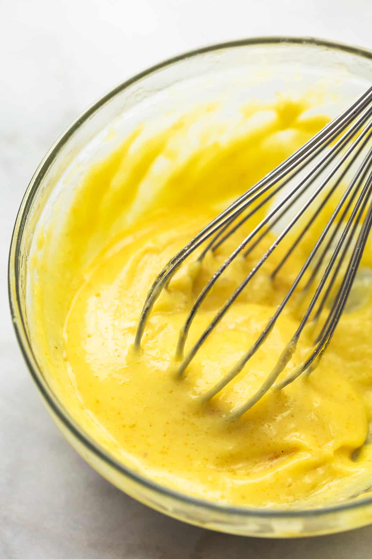 thickened yellow sauce with whisk in a glass bowl