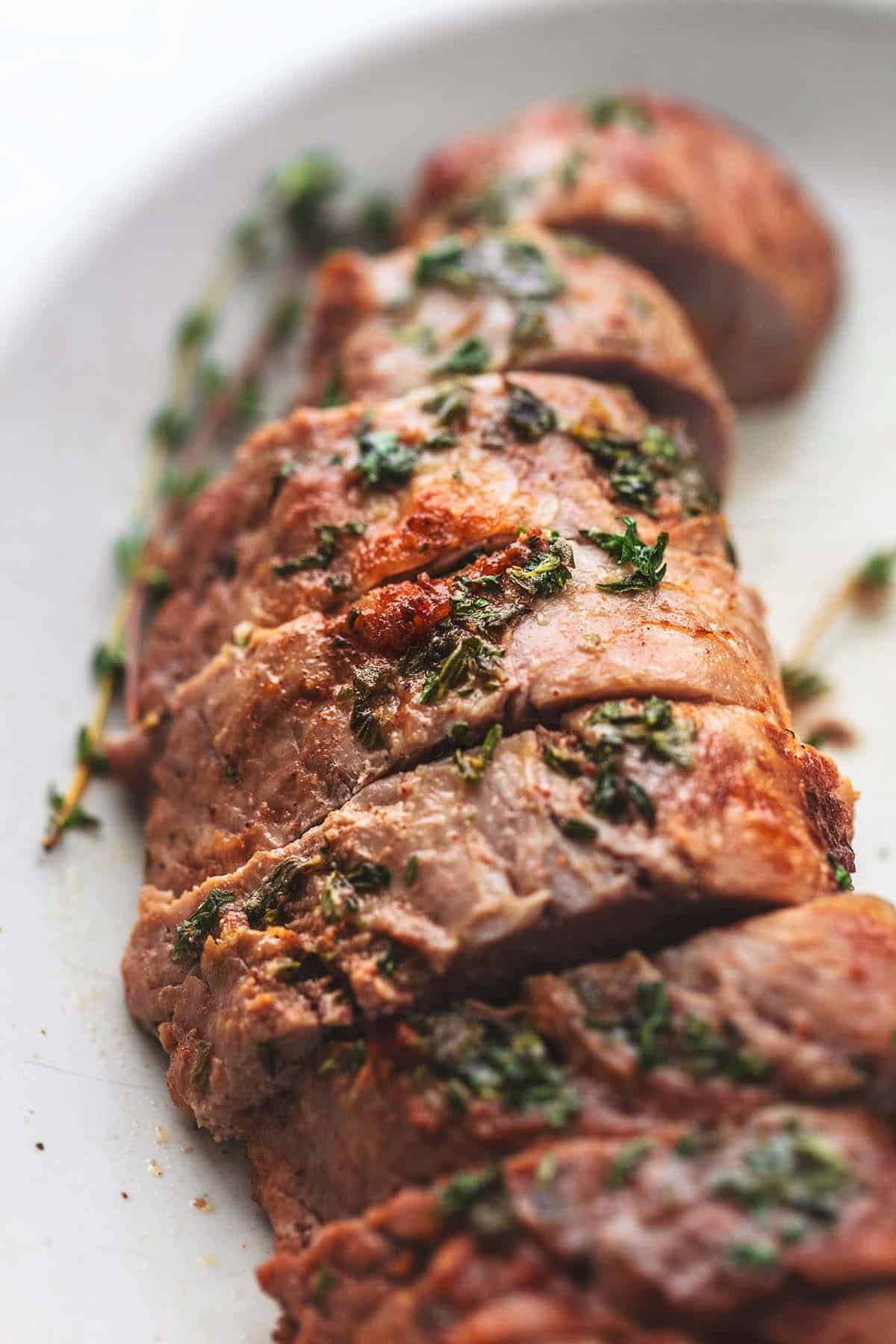 close up ofgarlic butter roasted pork tenderloin with herbs on top.