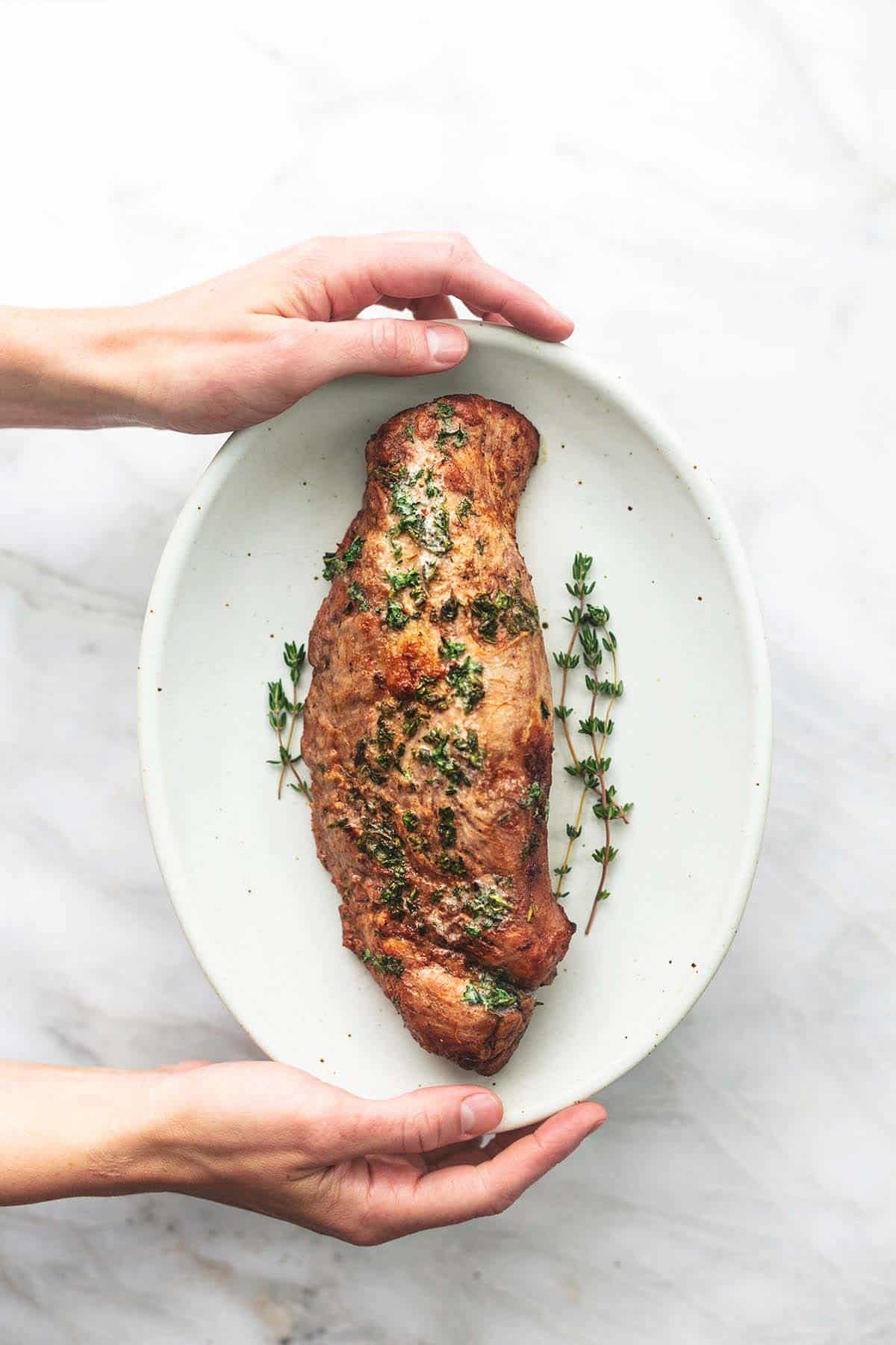 top view of hands holding a platter of garlic butter roasted pork tenderloin.