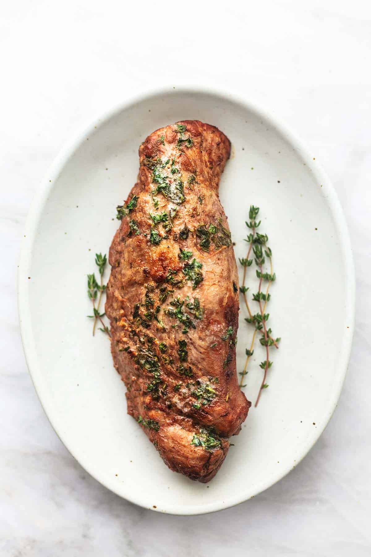 top view of garlic butter roasted pork tenderloin with fresh herbs on platter.