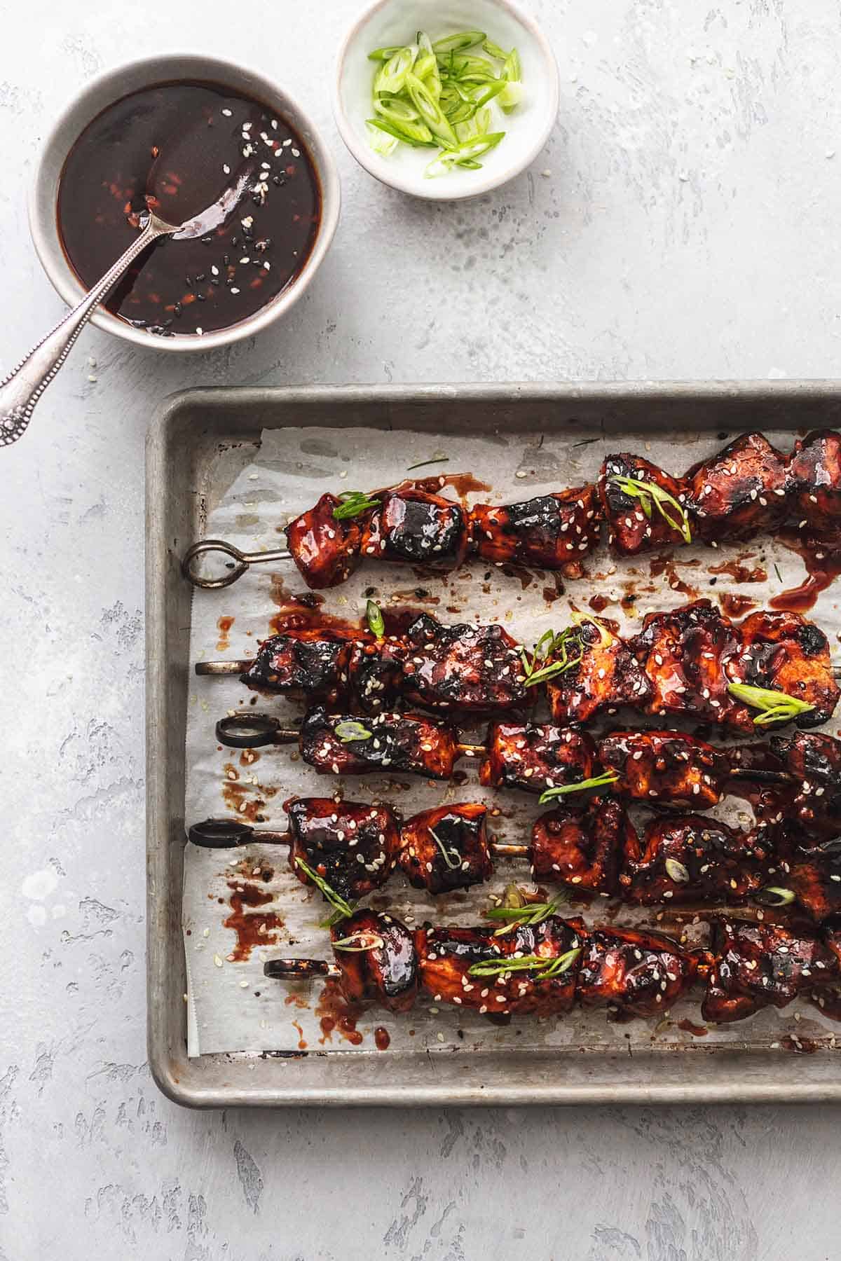 top view of Korean bbq chicken skewers on a baking sheet with two small bowls of condiments on the side.