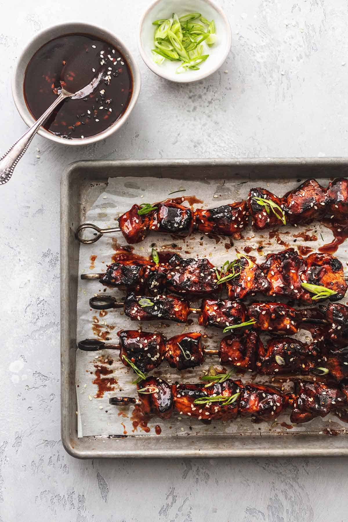 overhead view of chicken skewers on baking sheet and two small bowls of condiments