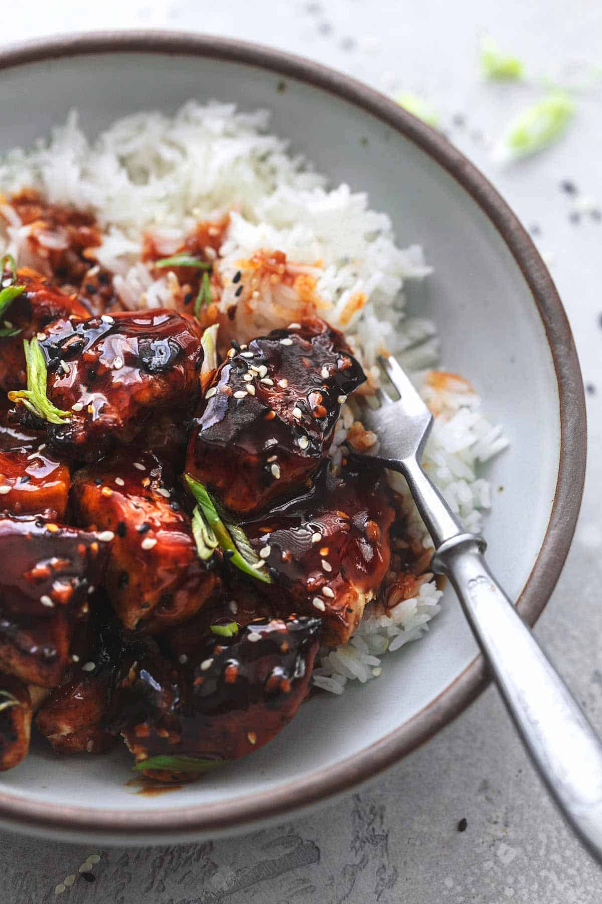 close up of Korean bbq chicken with rice and a fork in a bowl.