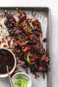 overhead view of chicken on skewers on sheet pan with bowl of sauce