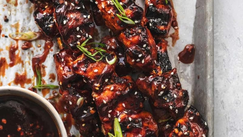 overhead view of chicken on skewers on sheet pan with bowl of sauce