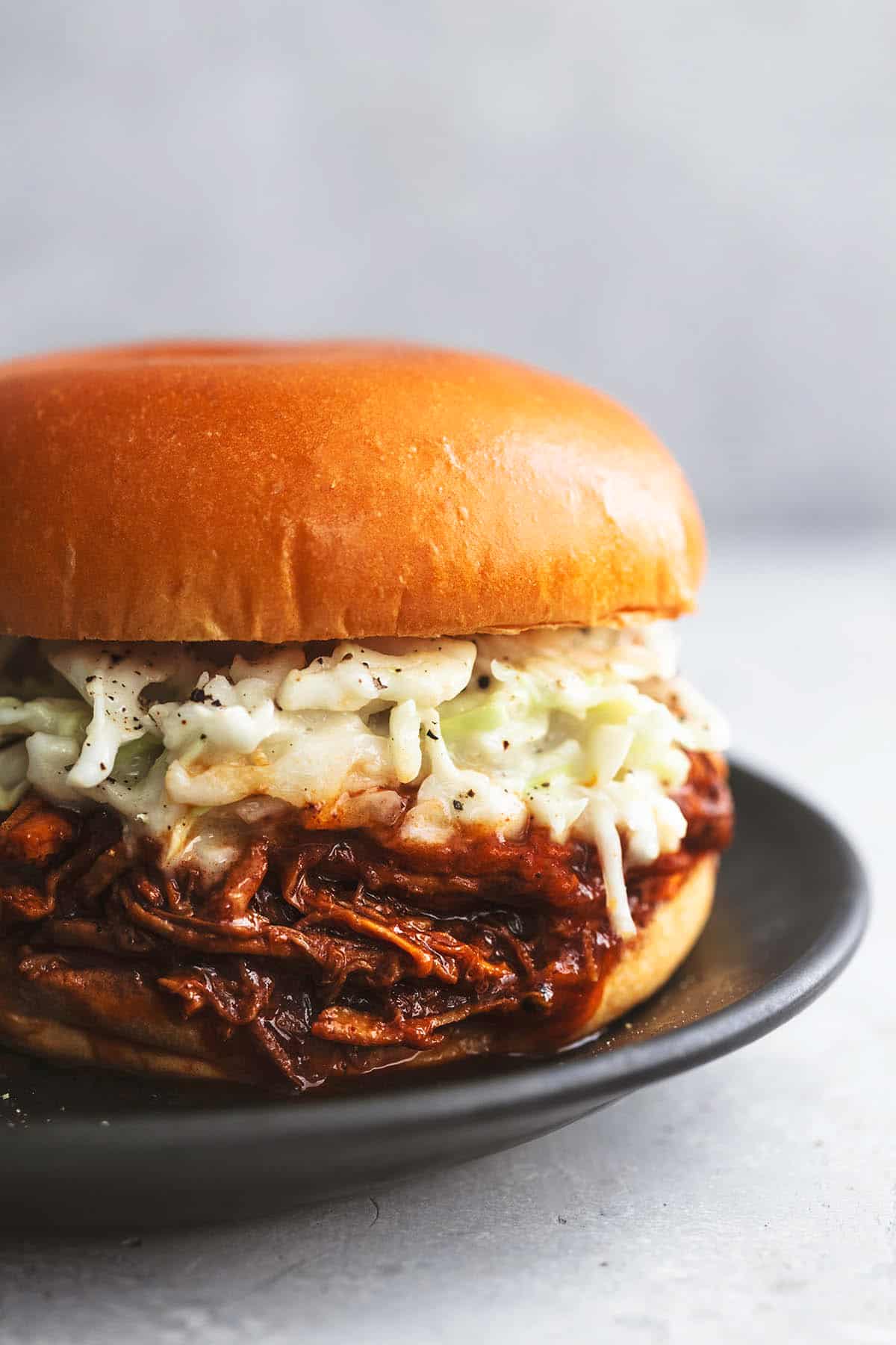 close up of a pulled pork sandwich with coleslaw on it on a plate.