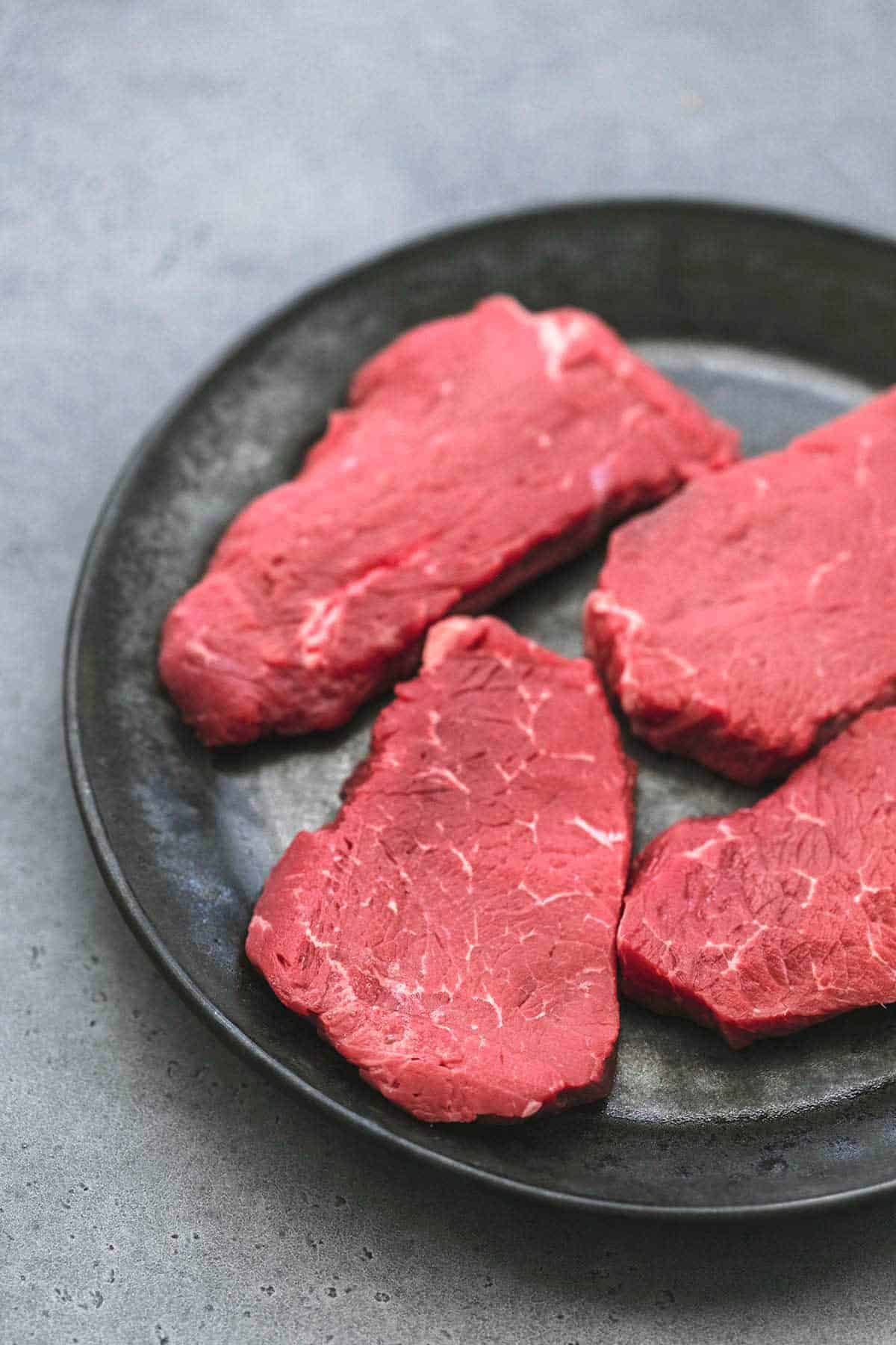 close up of whole pieces of raw sirloin steak on a plate.