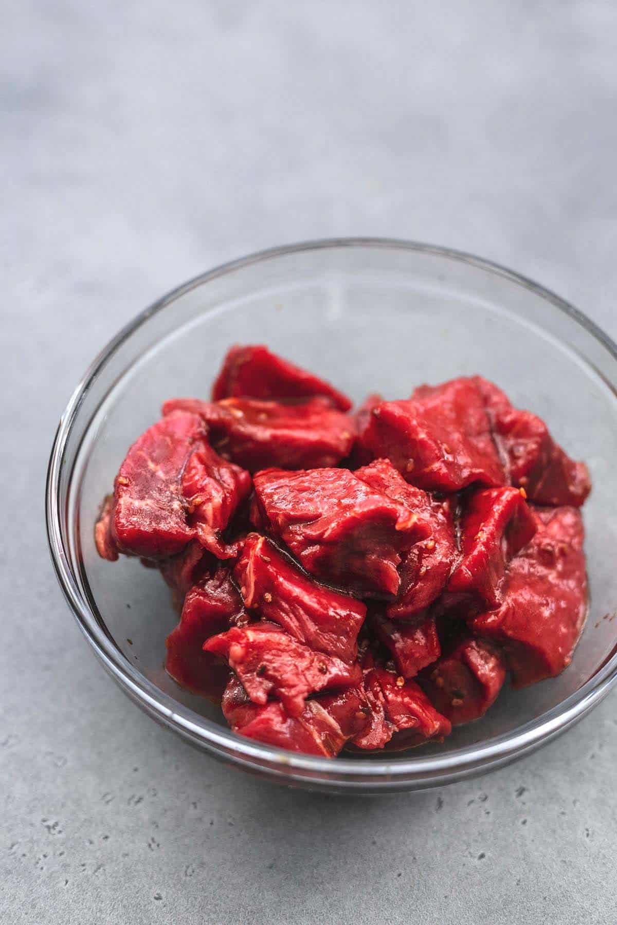 raw steak pieces tossed in dark sauce in a glass bowl.