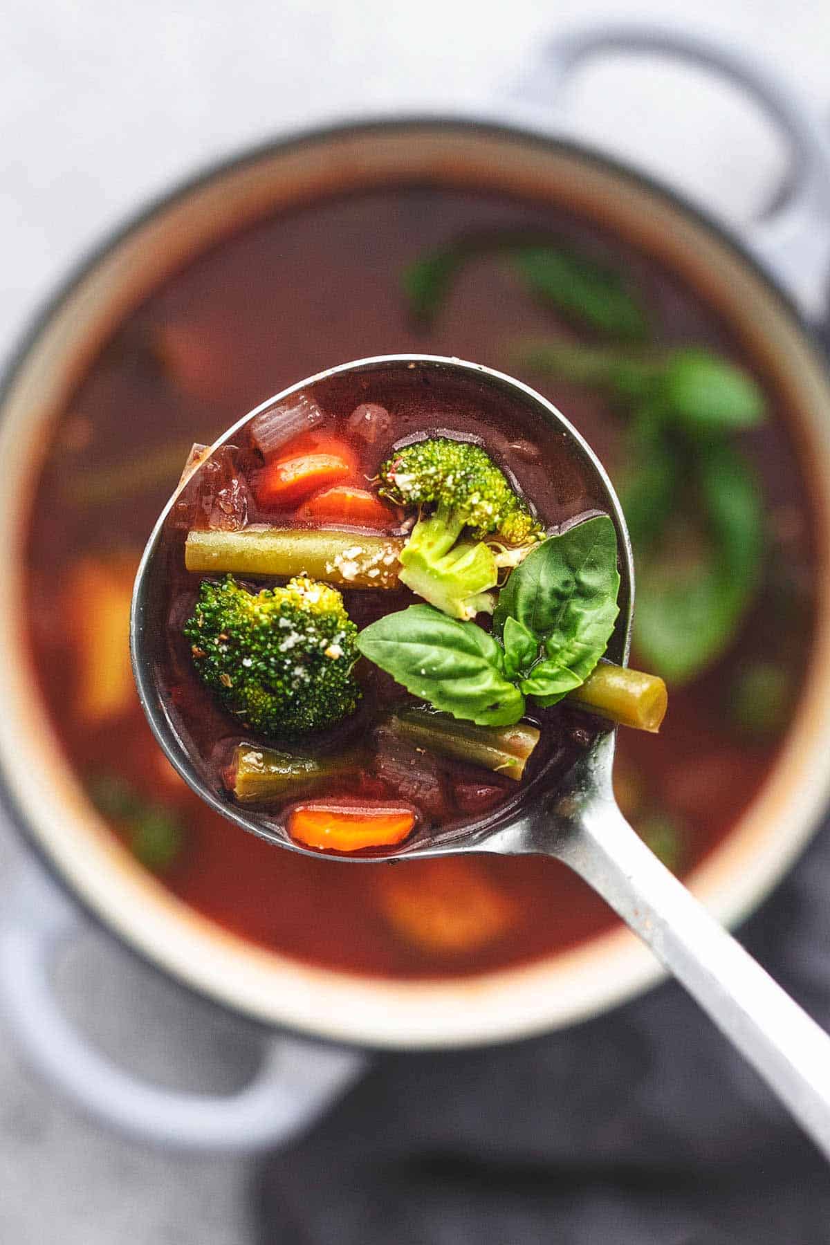 top view of a ladle full of vegetable soup being held up above a pot.