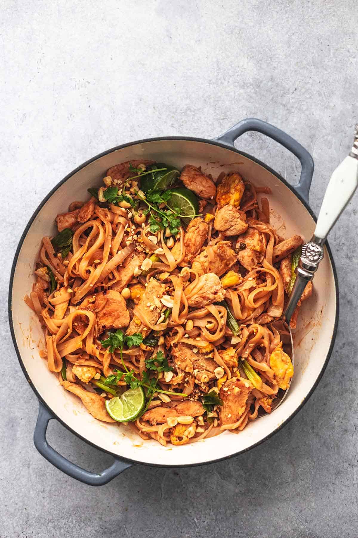 overhead view of serving spoon in skillet with cooked chicken pieces and noodles with fresh cilantro