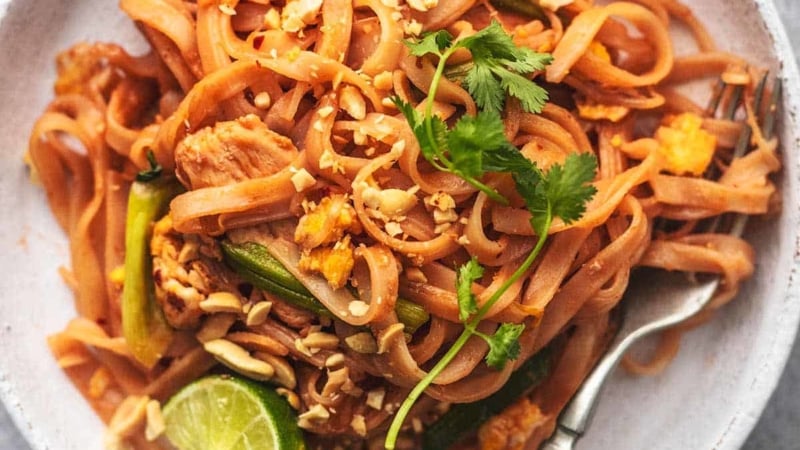 overhead closeup view of chicken pad thai on a white plate with a fork
