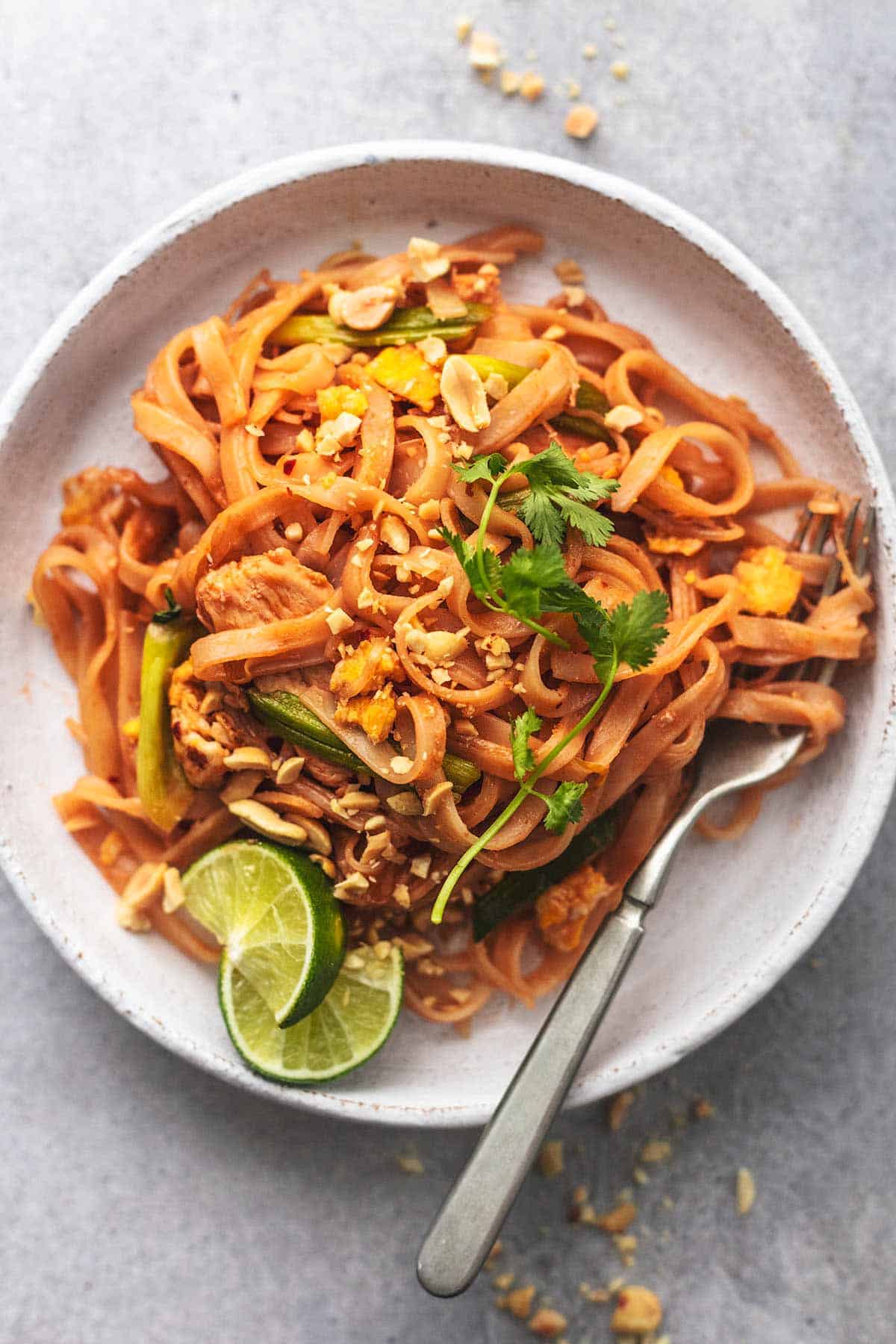 overhead closeup view of chicken pad thai on a white plate with a fork