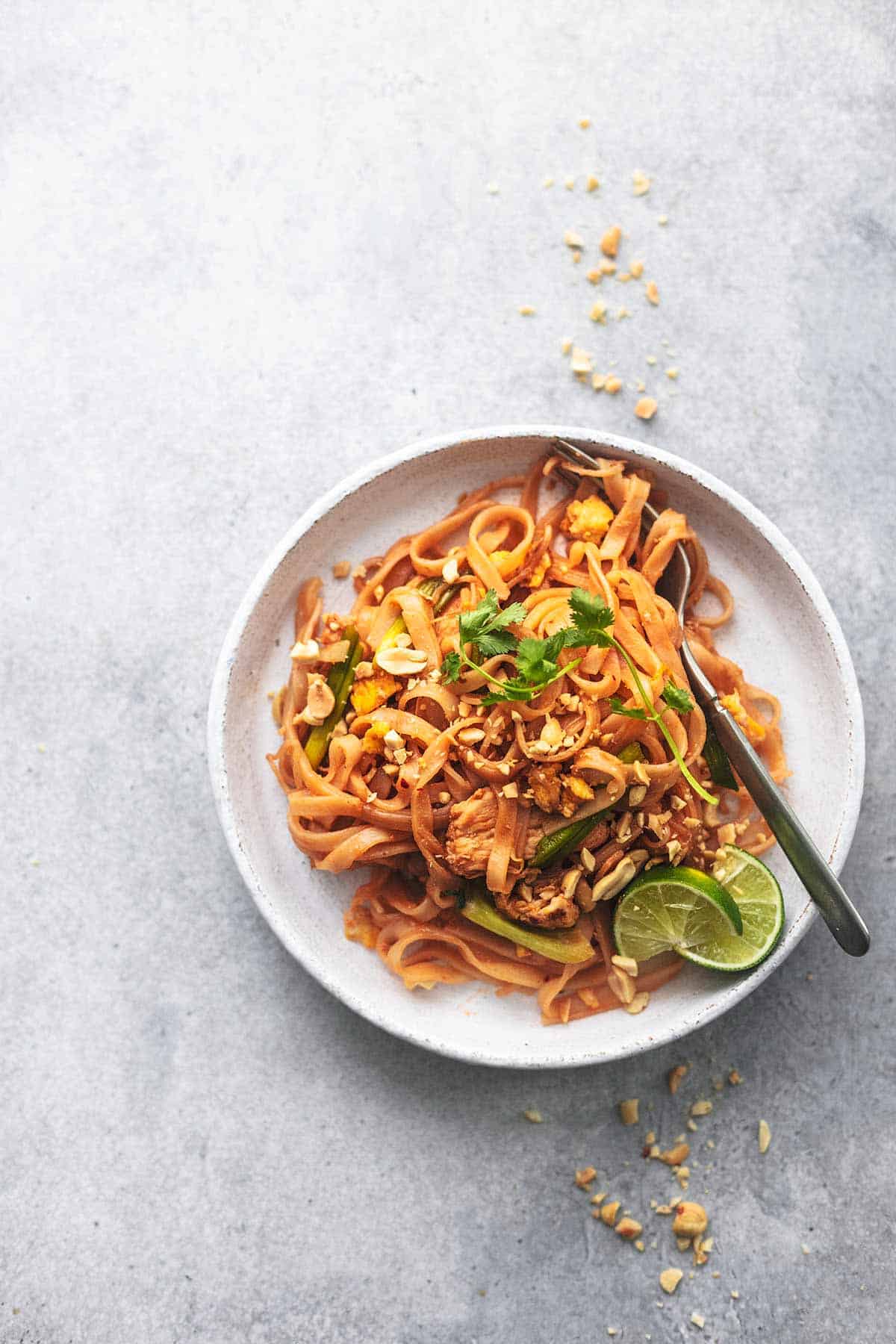 top view of a white plate with chicken pad Thai and a fork on it.