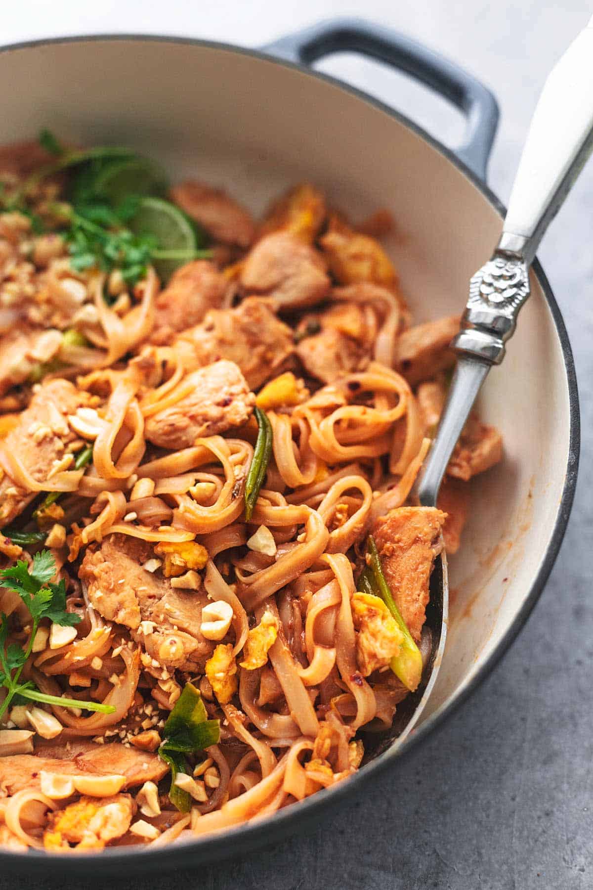 close up of chicken pad Thai and cilantro in a skillet with a serving spoon.