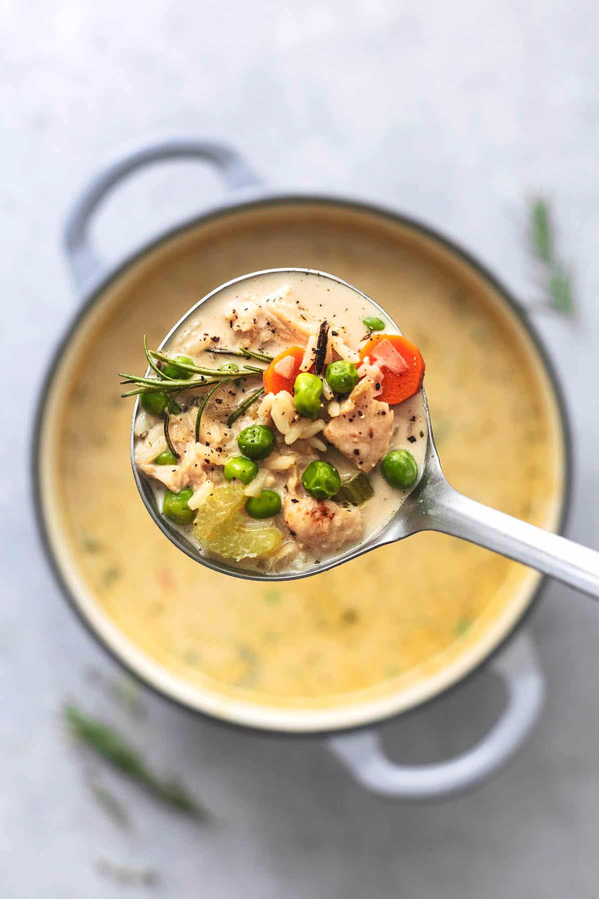 top view of a ladle full of chicken and rice soup being held above a pot.